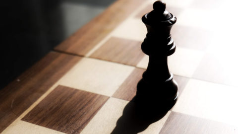 Chess black stands on chess board against the light source with shadow reflected on chess board.