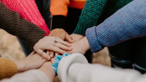 Hands of a multiracial group are put together in the center of the photo.