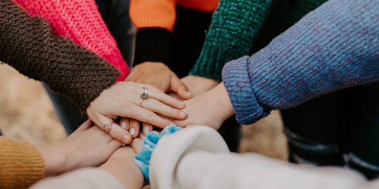 Hands of a multiracial group are put together in the center of the photo.