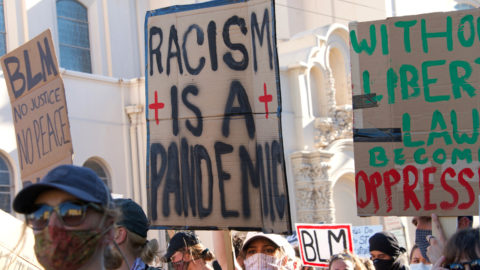 Protestors raise sign on racism and BLM.