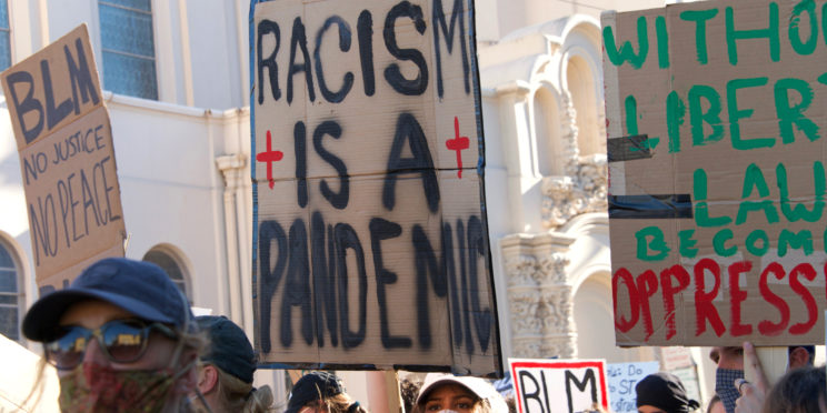 Protestors raise sign on racism and BLM.