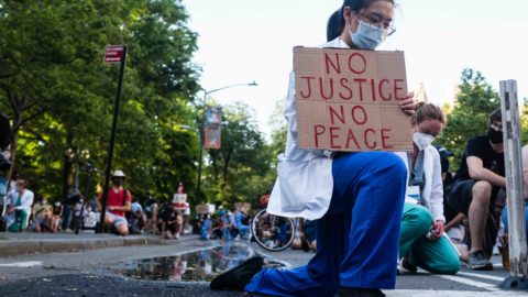 A health care professional kneels in protest as part of the movement, 'White Coats for Black Lives,' during the COVID-19 pandemic.