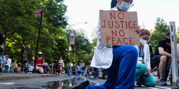 A health care professional kneels in protest as part of the movement, 'White Coats for Black Lives,' during the COVID-19 pandemic.