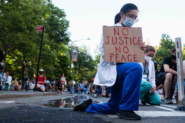 A health care professional kneels in protest as part of the movement, 'White Coats for Black Lives,' during the COVID-19 pandemic.