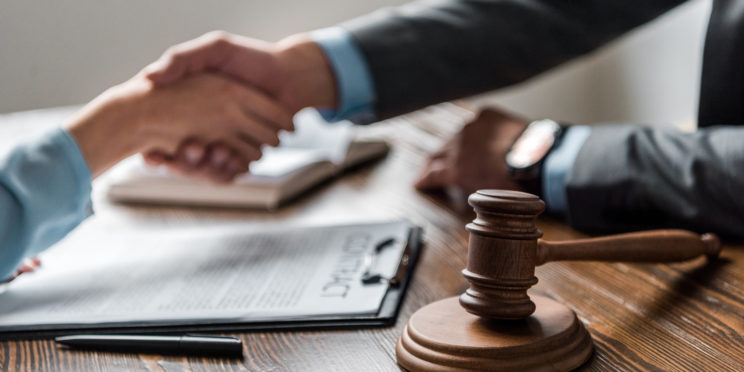 gavel in foreground of client and attorney shaking hands