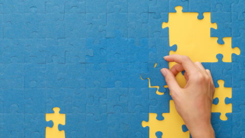 crop-view of a person's hand matching a blue puzzle on background
