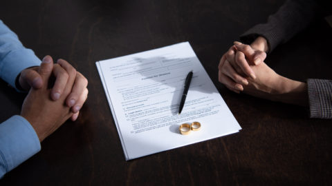 couple sitting at table with clenched hands near divorce documents and rings