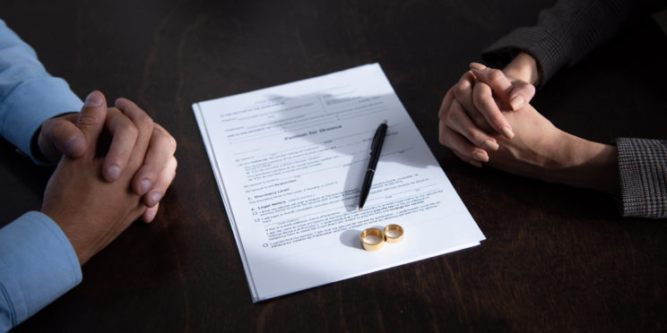 couple sitting at table with clenched hands near divorce documents and rings