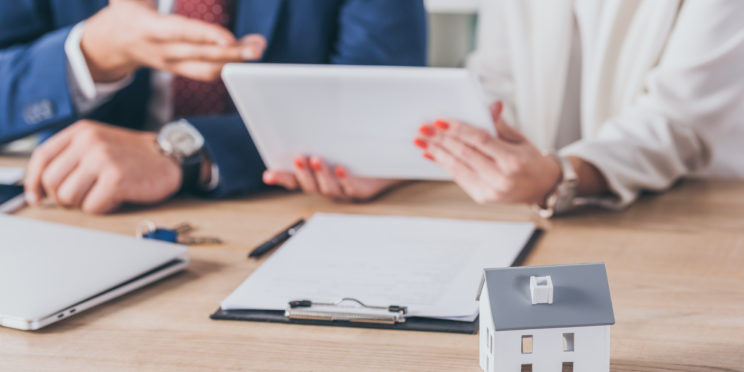 Selective focus of house model near woman holding digital tablet and businessman pointing with hand