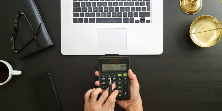 Lawyer is using calculator with scale and laptop on the desk.