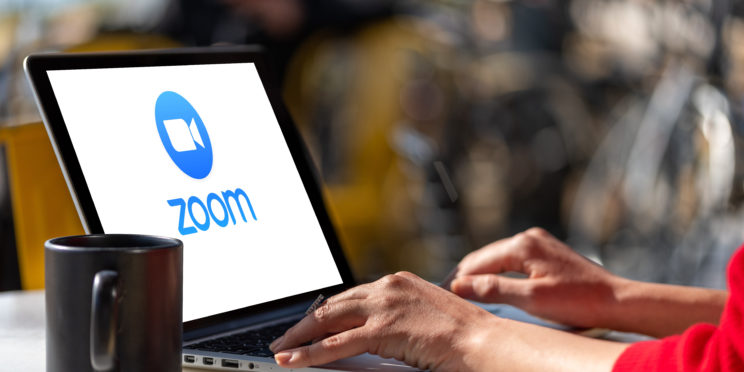 Woman using laptop showing Zoom Cloud Meetings app logo