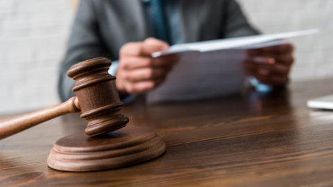 Close-up view of wooden hammer and judge working with documents behind