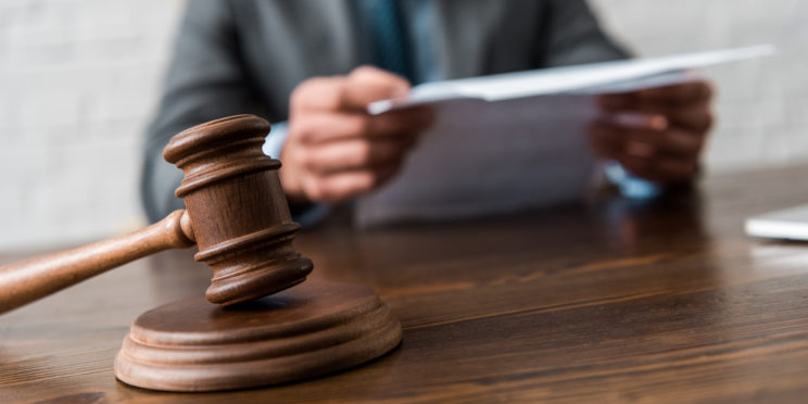 Close-up view of wooden hammer and judge working with documents behind